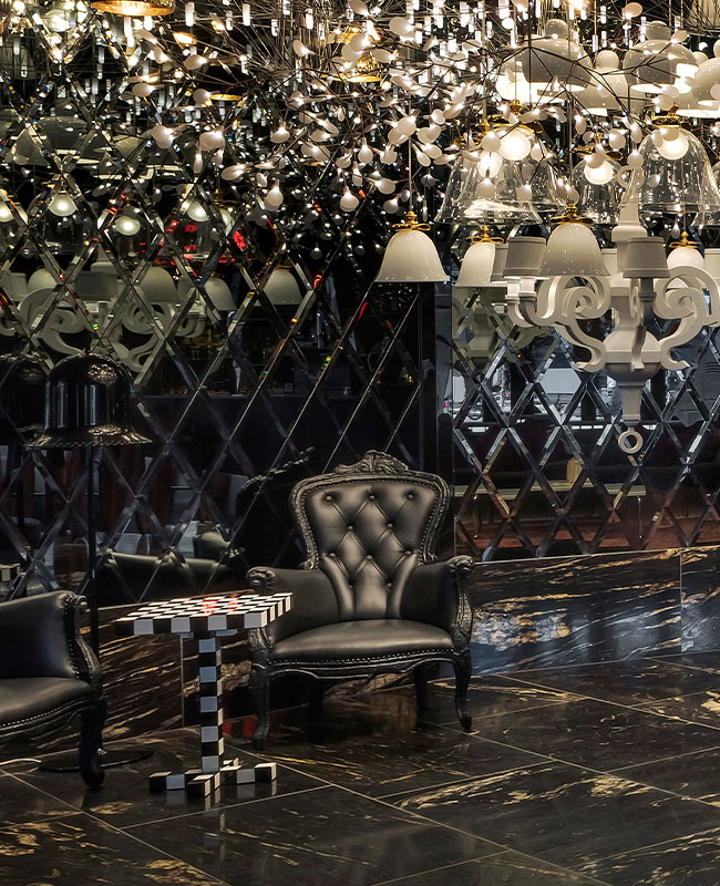A beautiful large chandelier hanging in a dark room above large black armchairs