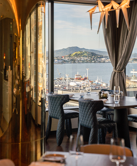 http://A%20four%20person%20restaurant%20table%20next%20to%20a%20large%20window%20over%20a%20large%20port%20with%20mountains%20in%20the%20background